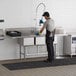 A man cleaning a Regency stainless steel 3 compartment sink in a kitchen.