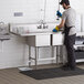 A man washing dishes in a Regency 2 compartment sink in a professional kitchen.