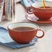 A close-up of an Acopa Sedona Orange stoneware cup of tea on a saucer.