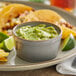 A plate with tortillas, limes, and a bowl of guacamole on a table.