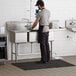 A man standing in a Regency stainless steel 3 compartment sink with a drainboard.