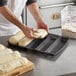 A person making bread in a Baker's Mark 5 compartment sub sandwich bread mold.