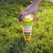 A hand holding a yellow container in the grass.