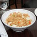 An American Metalcraft round melamine serving bowl filled with rice, chicken, and vegetables on a table.