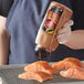 A woman pouring McCormick Grill Mates Seafood Seasoning onto raw salmon.