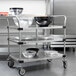 A Metro stainless steel utility cart with black bowls on a metal shelf.