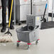 A man using a Lavex mop and bucket to clean a floor in a school kitchen.