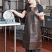 A woman in a brown San Jamar vinyl apron holding plates over a dishwasher.