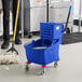 A man using a Lavex blue mop bucket to clean a floor.