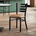 A Lancaster Table & Seating black ladder back chair with light brown vinyl padded seat.