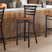 A ladder back bar stool with a distressed copper finish and an antique walnut wood seat.