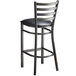A Lancaster Table & Seating black metal ladder back bar stool with a black vinyl cushion.