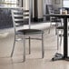 A Lancaster Table & Seating ladder back chair with a black vinyl padded seat.