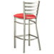 A Lancaster Table & Seating metal bar stool with a red vinyl padded seat.