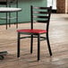 A Lancaster Table & Seating black finish ladder back chair with a mahogany seat on a wooden floor next to a table.
