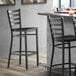 A Lancaster Table & Seating black ladder back bar stool with a black wood seat and metal frame.