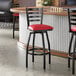 A black ladder back swivel bar stool with a red vinyl padded seat.