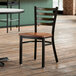 A Lancaster Table & Seating ladder back chair with a wooden seat sits on a wood floor in a restaurant dining area.