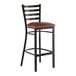A metal bar stool with a ladder back design and a burgundy vinyl padded seat.