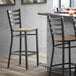 A Lancaster Table & Seating black metal ladder back bar stool with a driftwood seat.