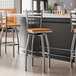 Lancaster Table & Seating Clear Coat Finish Ladder Back Swivel Bar Stools with Cherry Wood Seats at a bar counter.