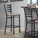 A Lancaster Table & Seating ladder back bar stool with a driftwood seat next to a table.