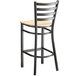 A black metal Lancaster Table & Seating bar stool with a natural wood seat and ladder back.