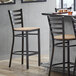 A Lancaster Table & Seating bar stool with a natural wood seat next to a table.