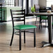 A black ladder back chair with a green vinyl padded seat and a distressed copper finish, placed in a dining area.
