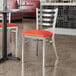 A Lancaster Table & Seating ladder back chair with a red vinyl padded seat at a table in a restaurant.