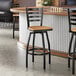 A black metal ladder back swivel bar stool with a natural wood seat.
