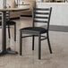 A Lancaster Table & Seating black metal chair with black vinyl padded seat at a table in a restaurant.