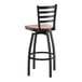 A black metal ladder back swivel bar stool with an antique walnut wood seat.