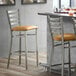 A Lancaster Table & Seating ladder back bar stool with a light brown vinyl cushion on a bar counter.