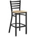 A Lancaster Table & Seating black ladder back bar stool with a natural wood seat.