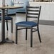 A Lancaster Table & Seating black ladder back chair with a navy vinyl padded seat next to a table in a restaurant.