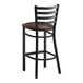 A Lancaster Table & Seating black ladder back bar stool with dark brown vinyl padded seat.