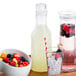A Tablecraft Swirl plastic carafe with a glass of liquid and a bowl of fruit on a table.