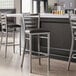 A Lancaster Table & Seating ladder back bar stool with a black vinyl padded seat.