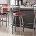 A group of Lancaster Table & Seating clear coat finish ladder back swivel bar stools with burgundy vinyl padded seats next to a counter.