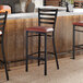 A ladder back bar stool with a distressed copper finish and a burgundy vinyl padded seat.