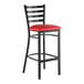 A black metal bar stool with a ladder back design and a red vinyl padded seat.