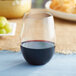 A Choice clear plastic stemless wine glass filled with red wine on a table next to grapes.