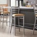 A group of Lancaster Table & Seating clear coat finish ladder back bar stools with light brown vinyl padded seats at a counter.
