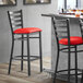 A Lancaster Table & Seating black ladder back bar stool with red vinyl padded seat.