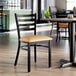 A black metal ladder back chair with a light brown vinyl padded seat, placed in a restaurant setting.