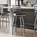 A group of Lancaster Table & Seating ladder back bar stools with black vinyl padded seats next to a counter.