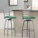 Two Lancaster Table & Seating metal bar stools with green vinyl padded seats.