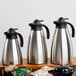 A close-up of a stainless steel Tablecraft coffee carafe with a black lid.