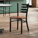 A Lancaster Table & Seating wooden chair with a black ladder back and antique walnut wood seat at a table in a restaurant dining area.